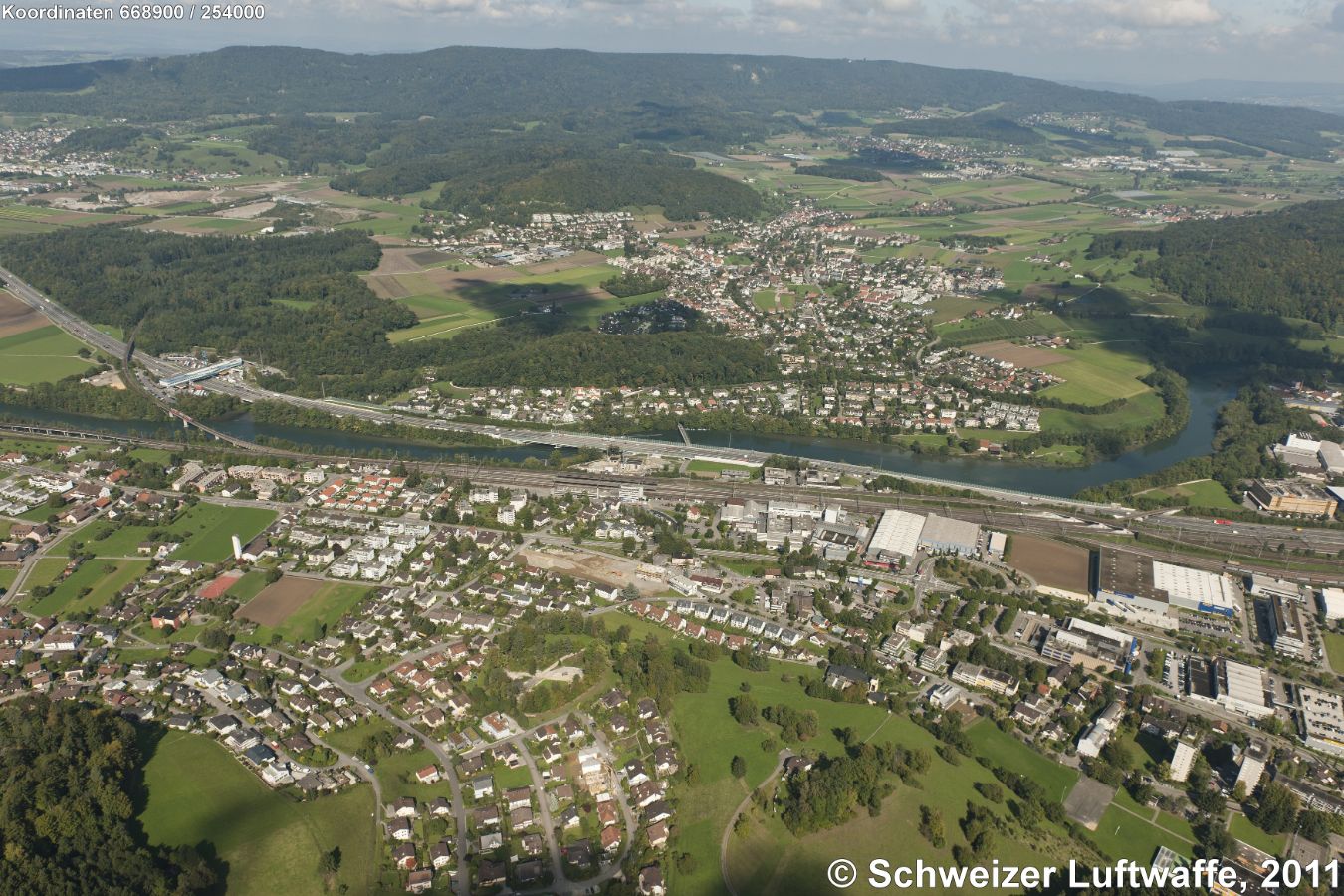 Killwangen (Vordergrund, links der Limmat) mit Bahnhof Killwangen-Spreitenbach und Würenlos (Bildmitte). Ganz links Bildmitte: Autobahnraststätte A1 'Würenlos', dahinter Wald 'Tägerhard'; linke Bildecke: Wettingen. Rechte obere Bildecke: Industriegebiet Otelfingen.